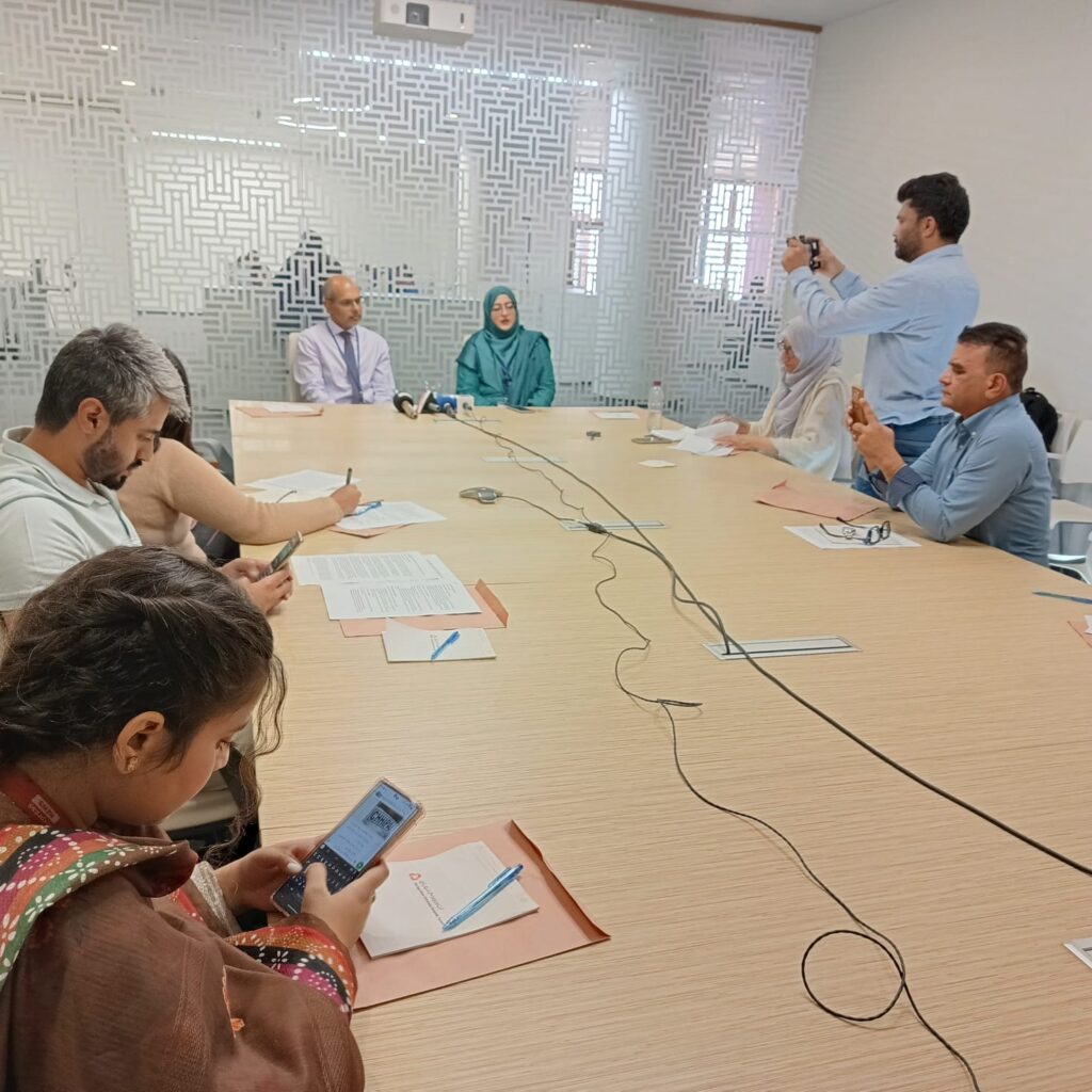Healthcare professionals discussing Nipah virus risk and public health preparedness during a medical briefing, with laboratory equipment and virus research visuals in a clinical conference setting.